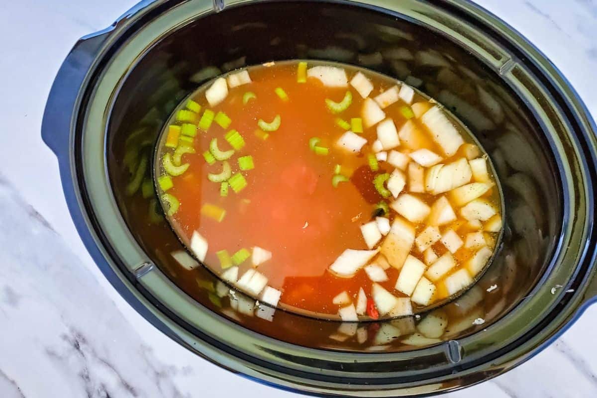 Crockpot filled with dry beans and vegetables soaking in broth and water.