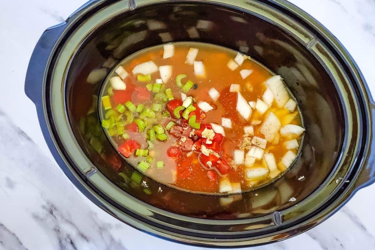 Crockpot filled with dry beans and vegetables soaking in broth and water.