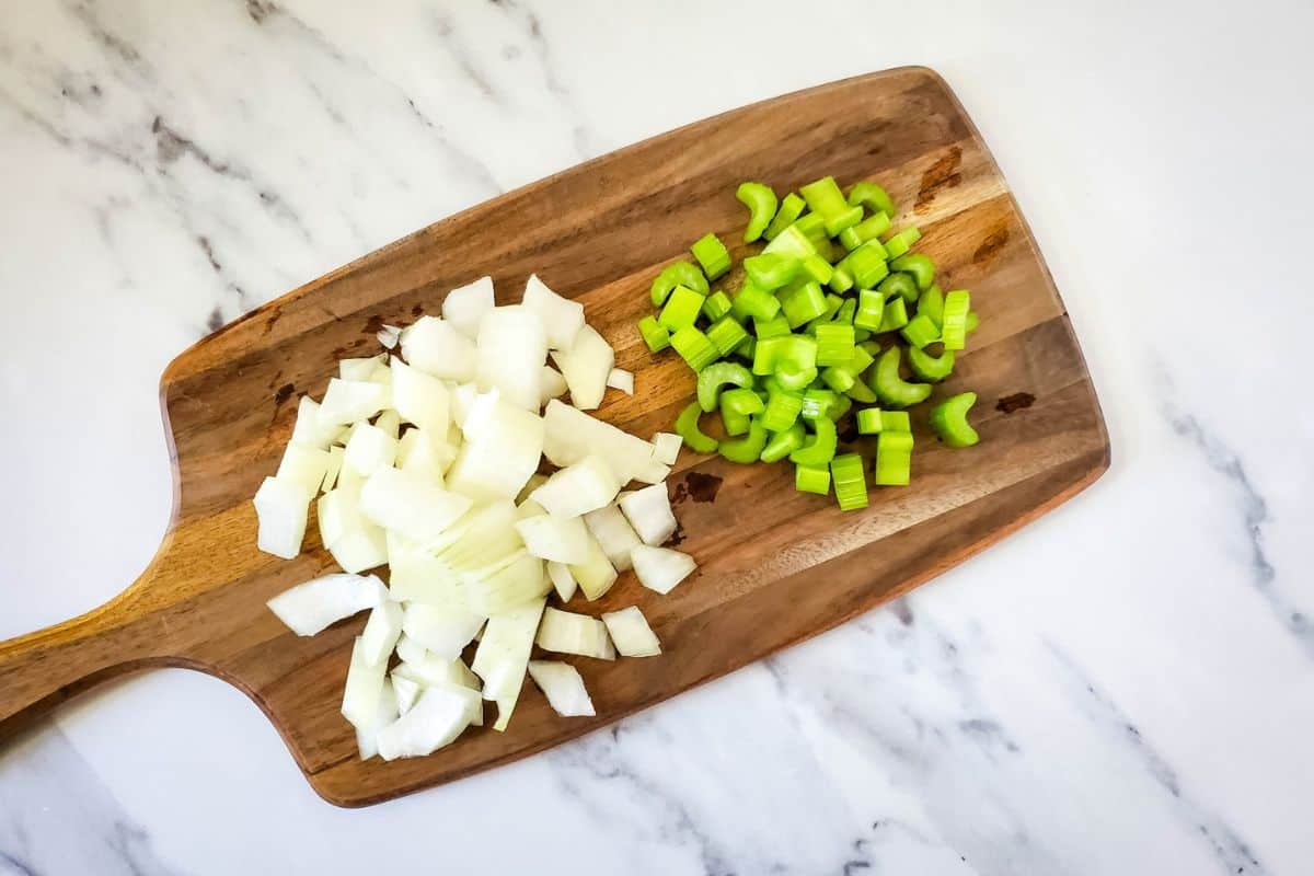 Onion and celery being chopped on a cutting board.