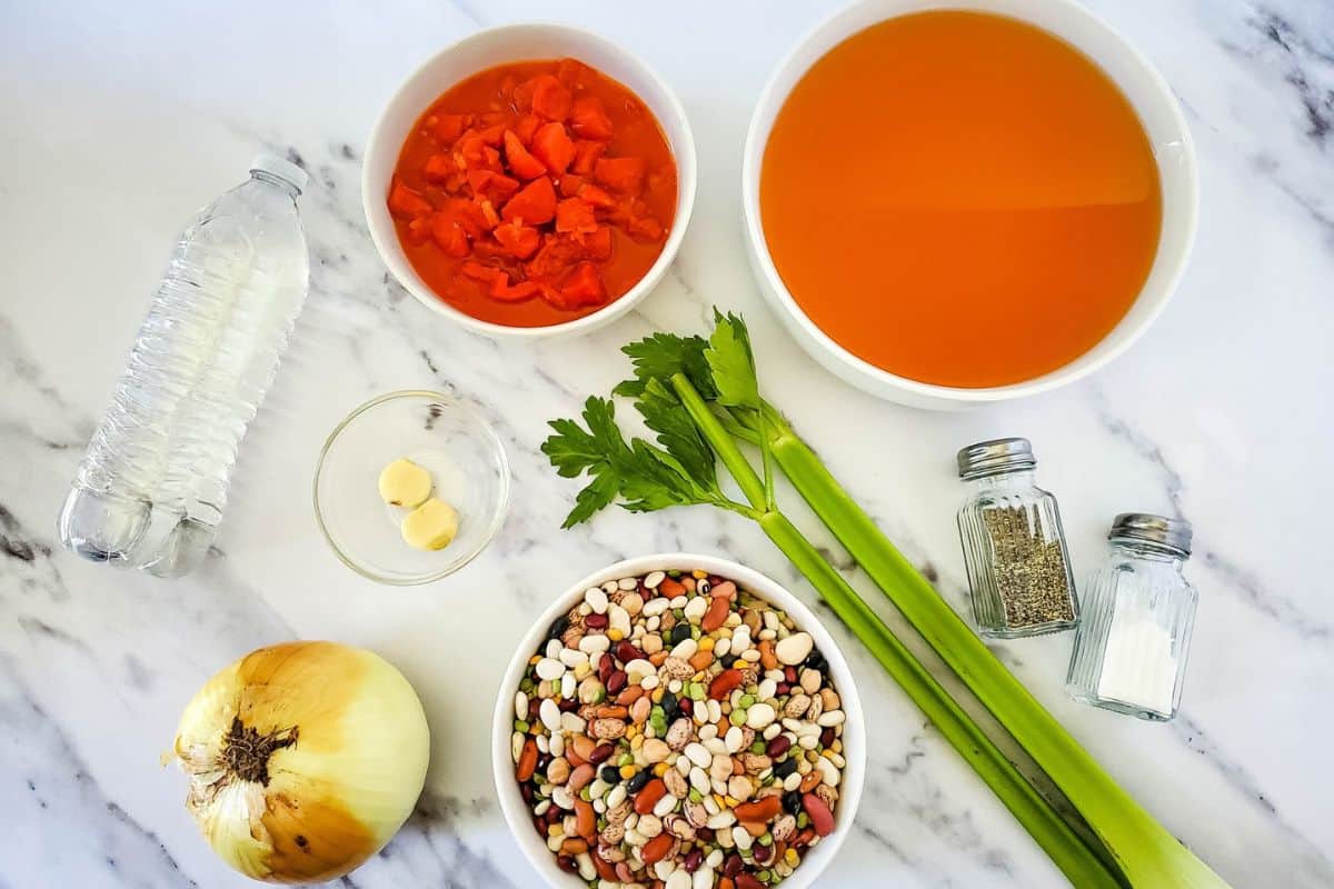 Ingredients for vegan bean soup arranged on a surface, including beans, vegetables, canned tomatoes, and seasonings.