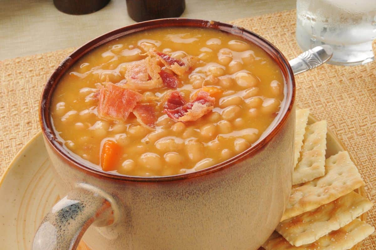A soup being placed into a crockpot with visible beans, broth, and chopped vegetables.