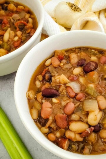 Two bowls of vegan bean soup on a table, filled with beans, vegetables, and broth.