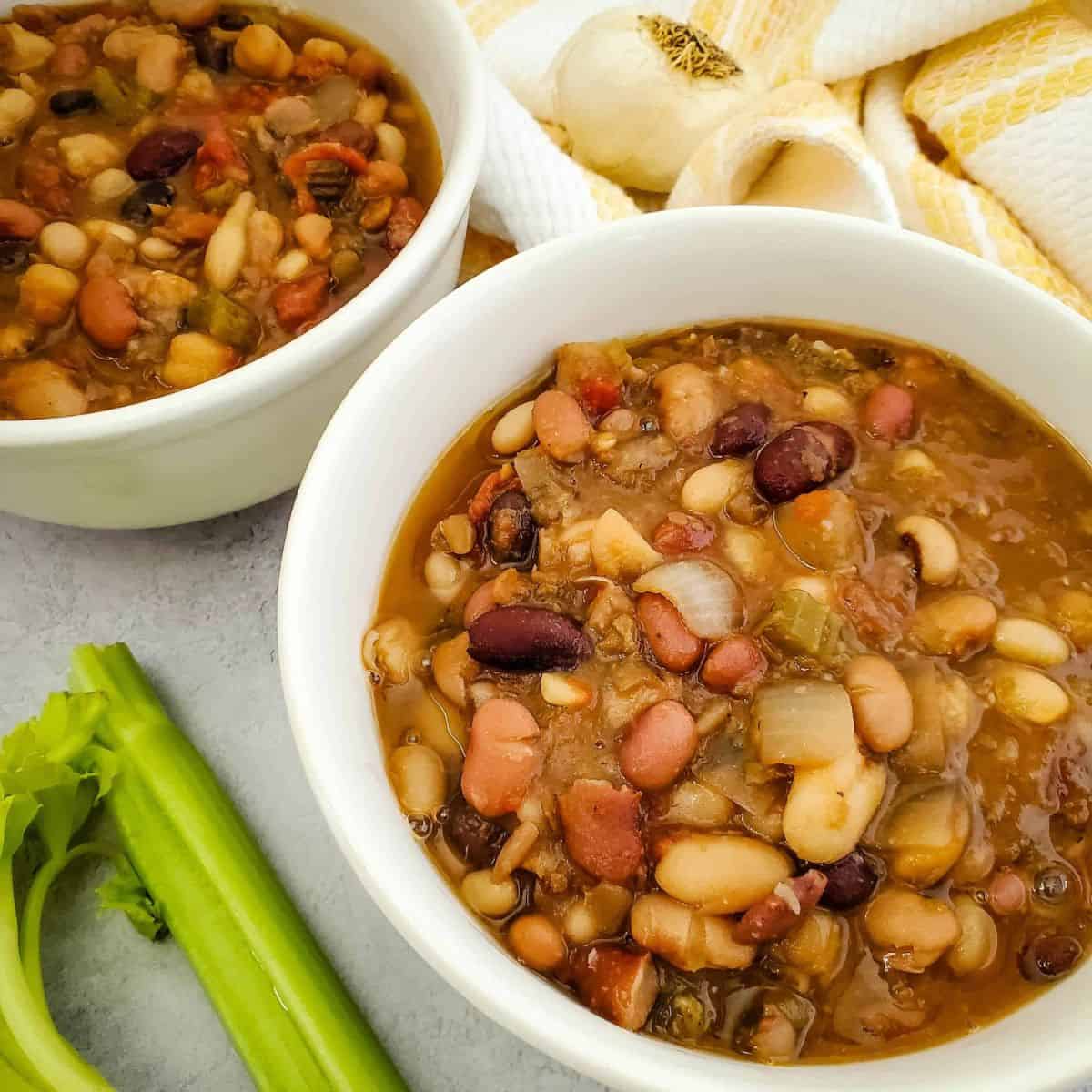 Two bowls of vegan bean soup on a table, filled with beans, vegetables, and broth.