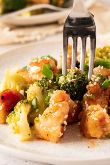 A fork pressed into juicy chicken on a plate, ready to lift.