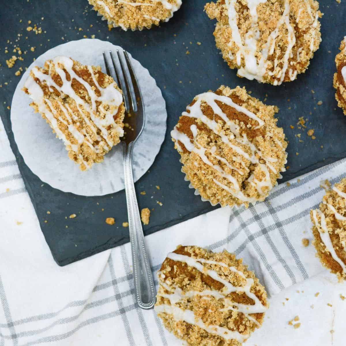 A single pumpkin streusel muffin with a fork beside it, surrounded by more muffins in the background.