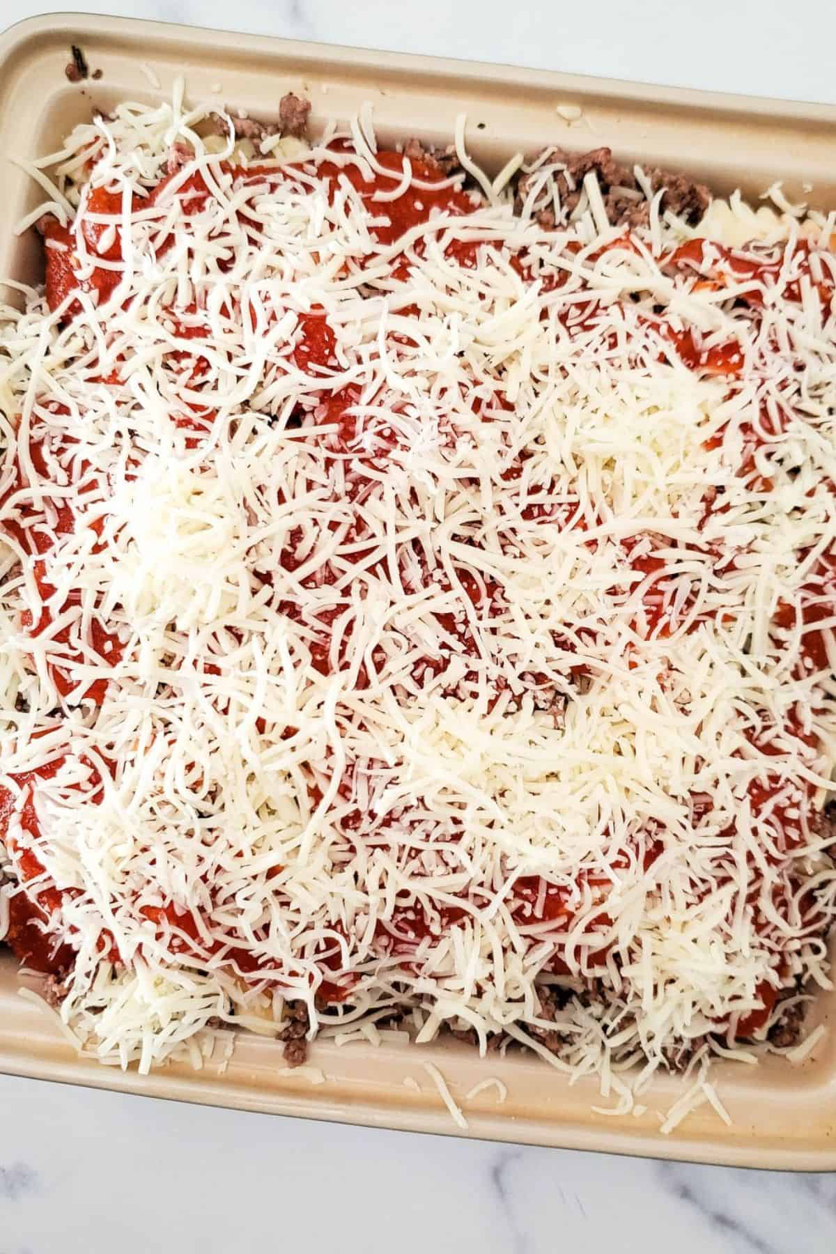 Ravioli served in a container, topped with shredded mozzarella cheese and red sauce.