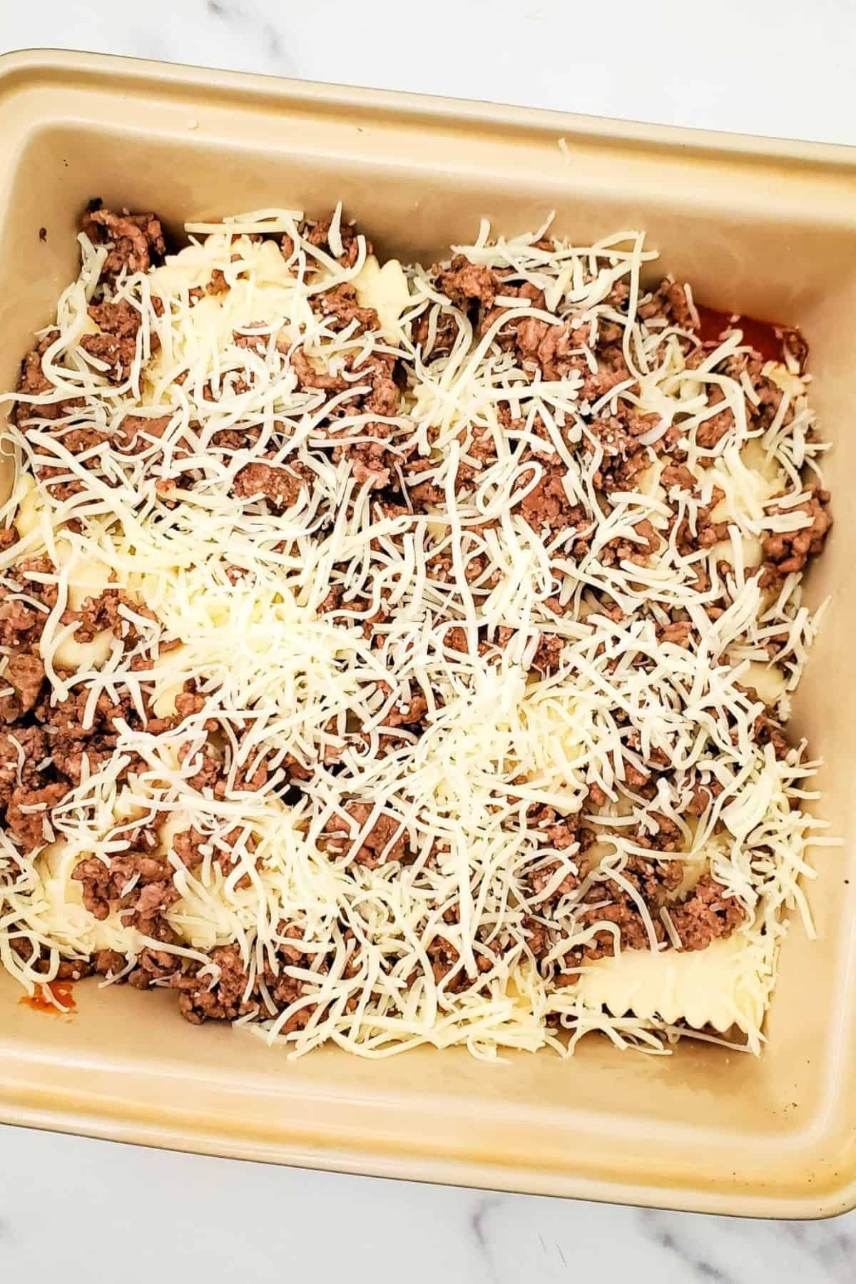 Ravioli served in a container, topped with shredded mozzarella cheese and red sauce.