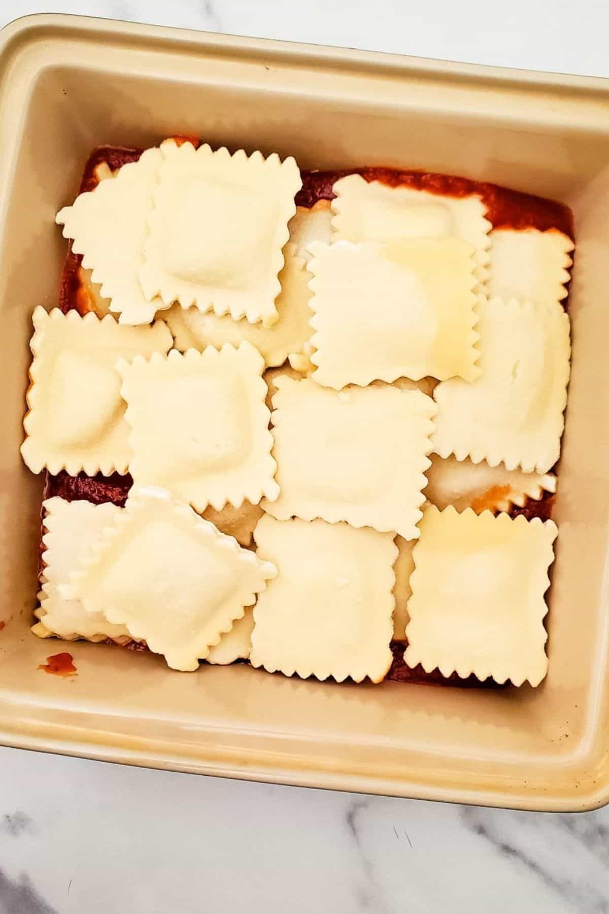 Ravioli in a container topped with red sauce and shredded cheese.