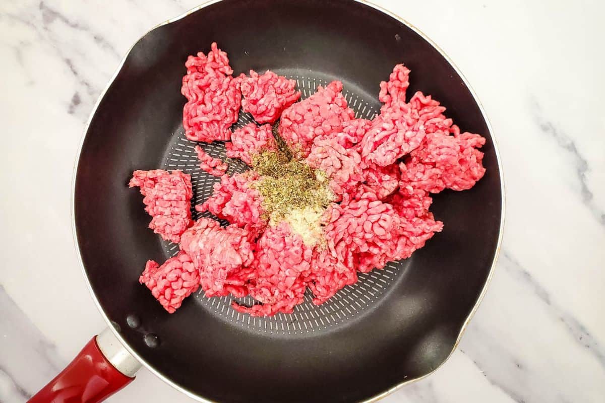 Ground beef cooking in a skillet with Italian seasoning and garlic powder.