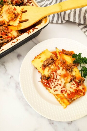 Ravioli lasagna on a plate with the baking dish and spatula in the background.