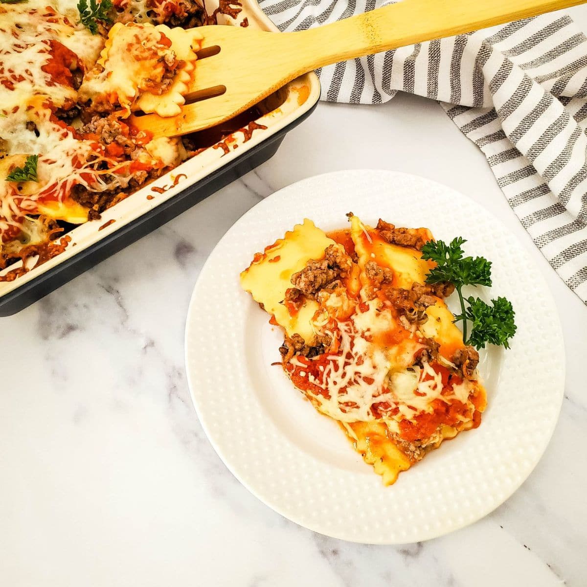 Ravioli lasagna on a plate with the baking dish and spatula in the background.