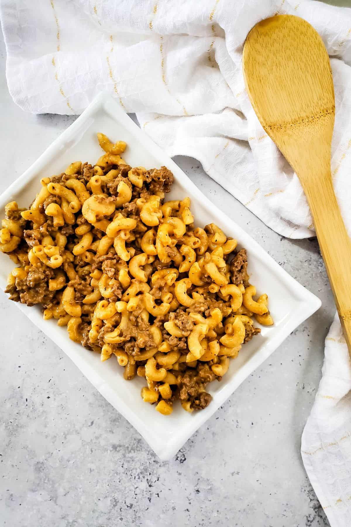 Macaroni served in a dish with a spatula and kitchen cloth beside it.