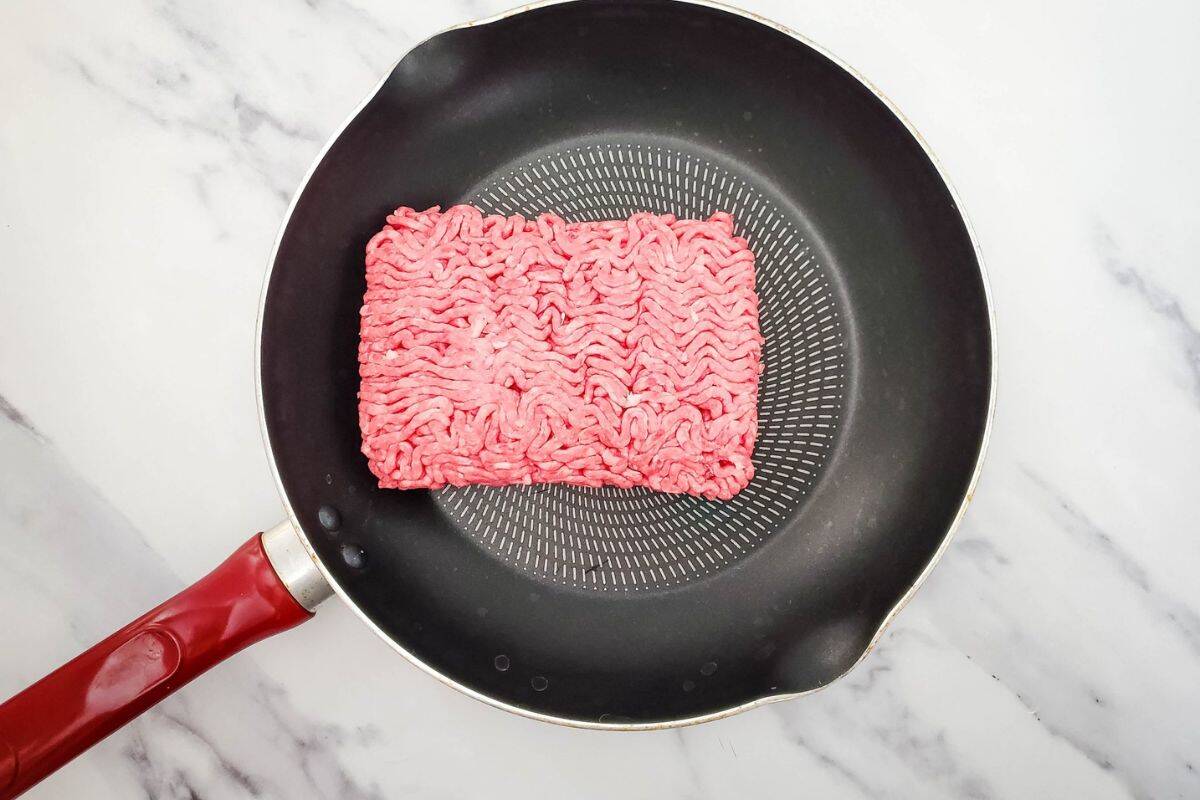Beef cooking in a hot skillet with juices around it.