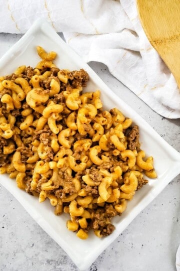 Macaroni served in a dish with a spatula and kitchen cloth beside it.