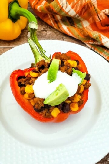 A single taco served on a white plate, with a colorful bell pepper blurred in the background.