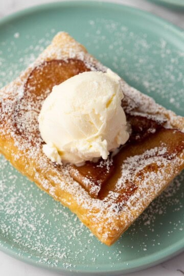Upside-down apple tart served on a plate, topped with powdered sugar and a scoop of vanilla ice cream.