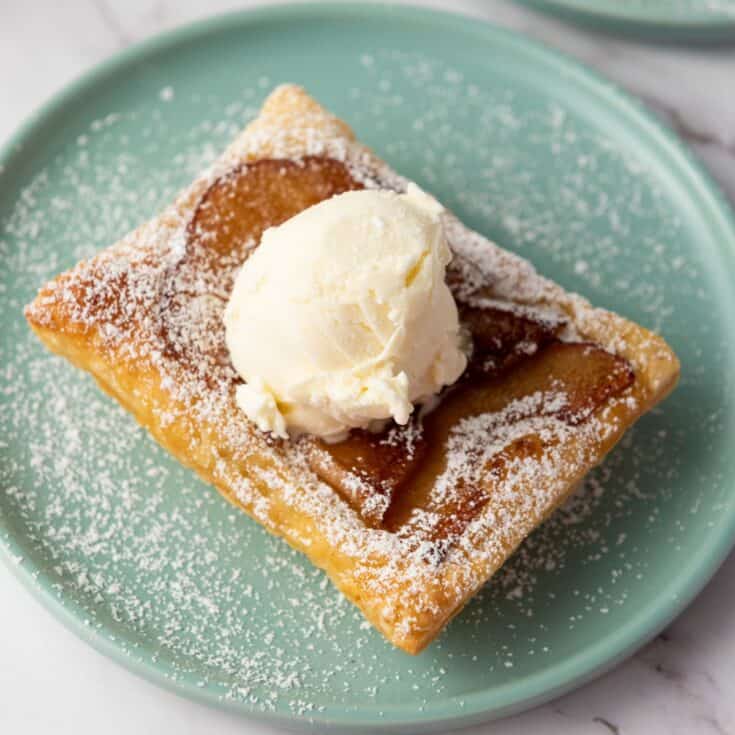 Upside-down apple tart served on a plate, topped with powdered sugar and a scoop of vanilla ice cream.