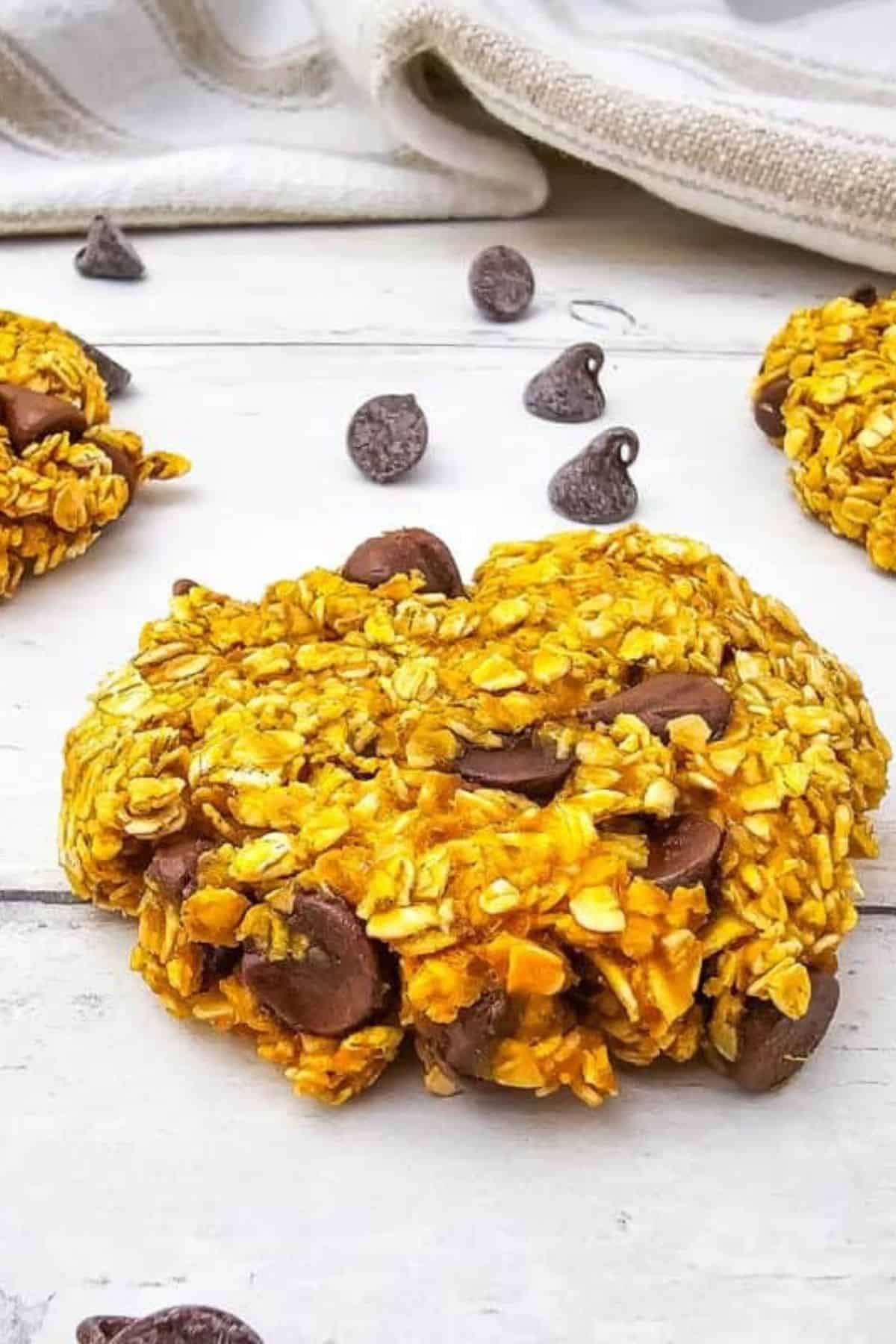 Pumpkin oatmeal cookies on a surface surrounded by scattered chocolate chips.