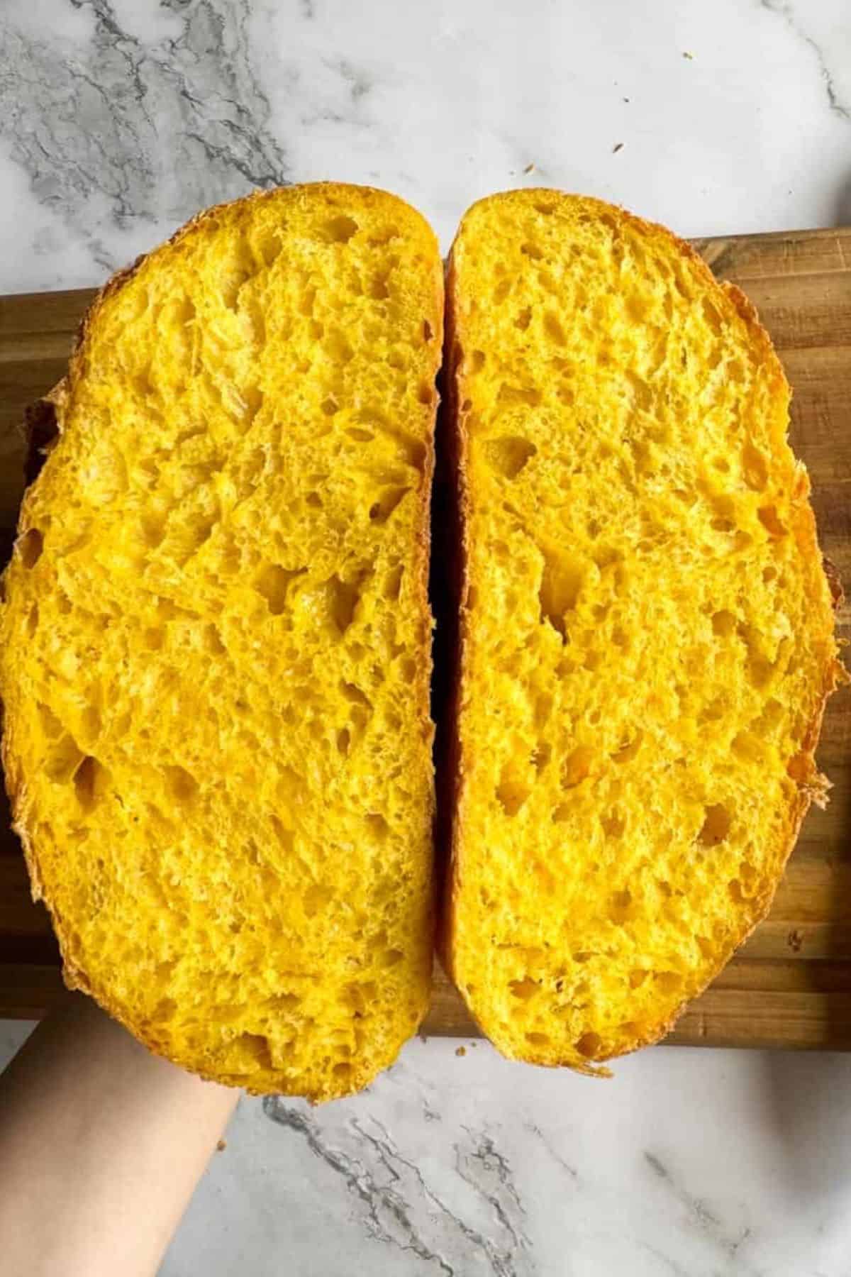 Fresh sourdough bread being sliced in half with a person holding it.