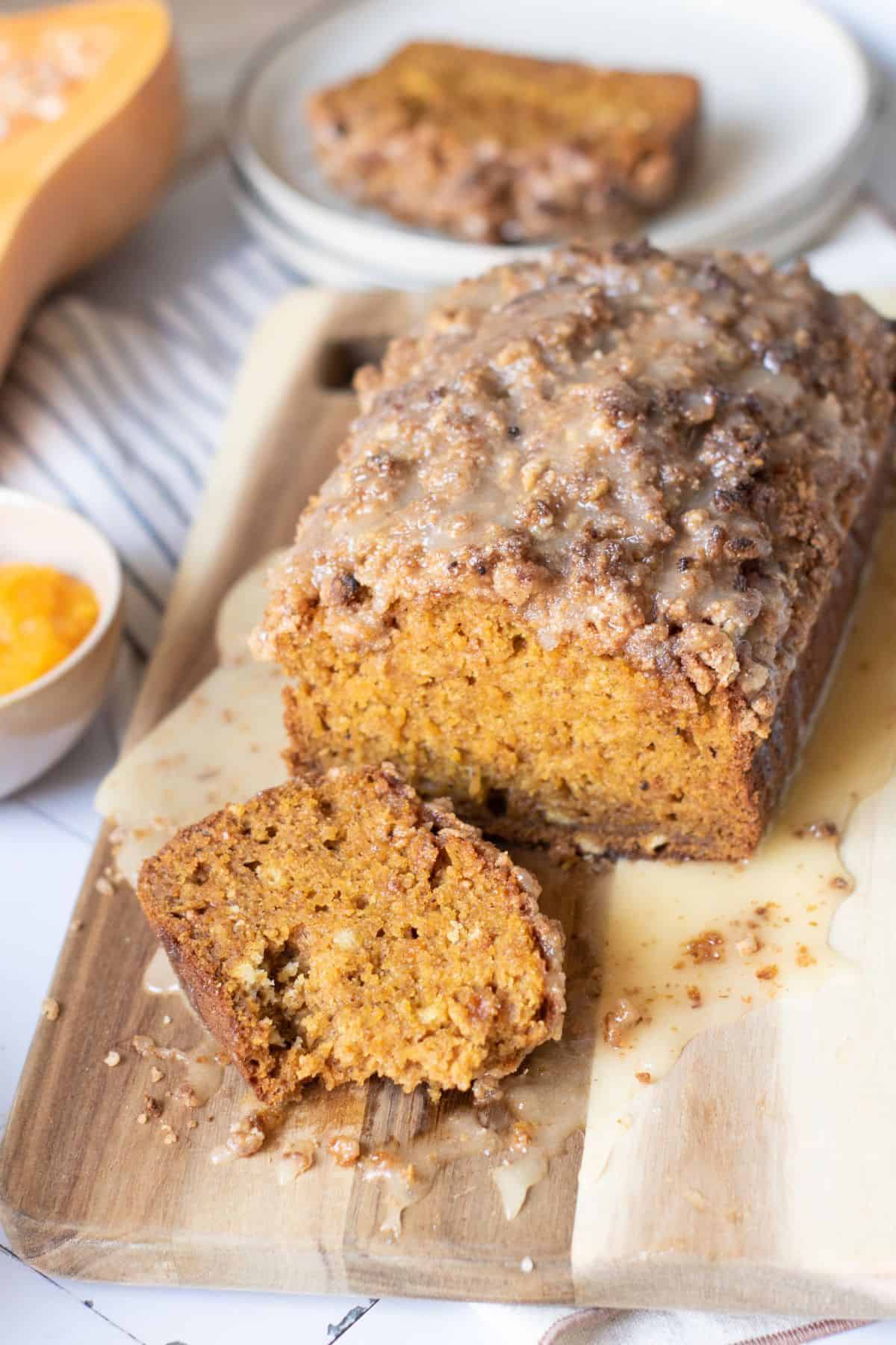 Pumpkin Bread with Streusel Topping and Honey Glaze being sliced, with the loaf placed beside the slices.