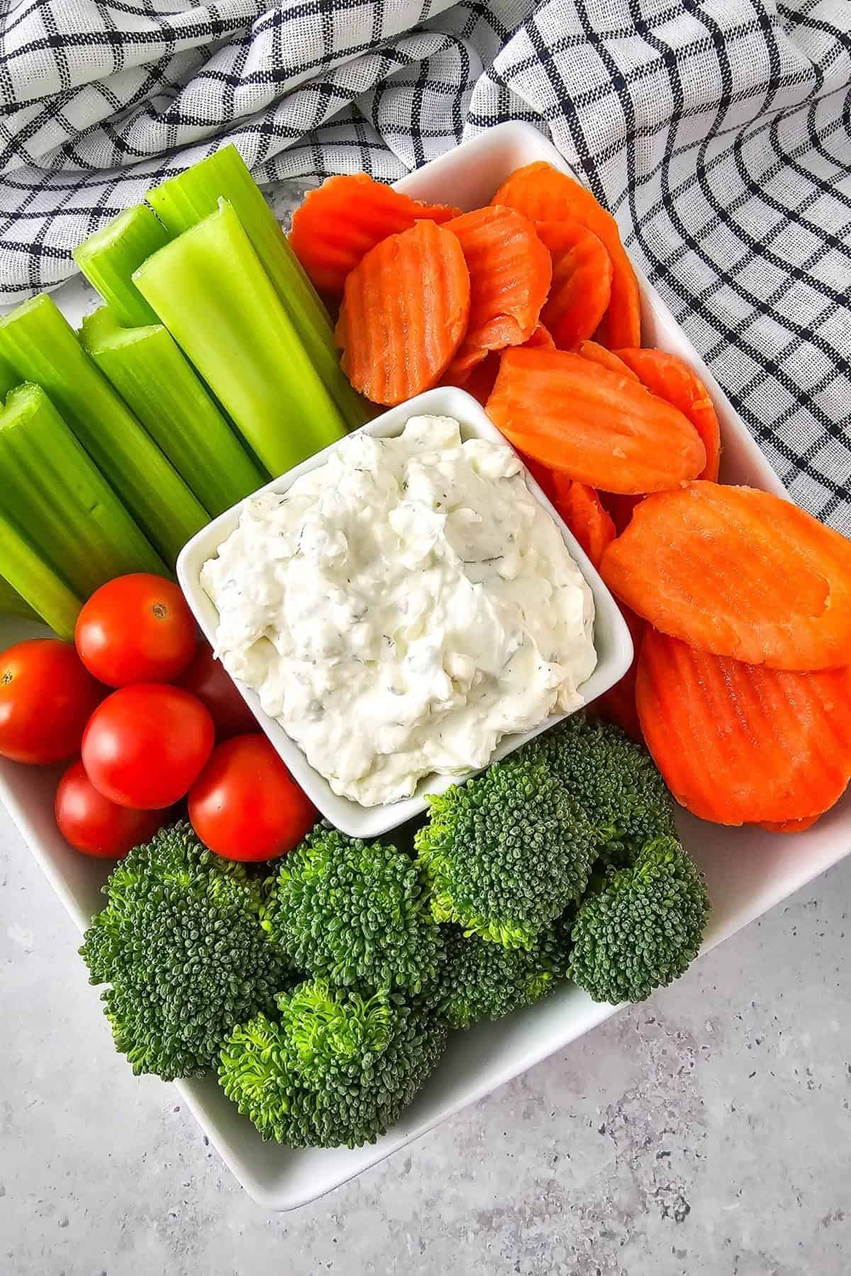 A bowl of creamy dip in the center, surrounded with an assortment of fresh vegetables.