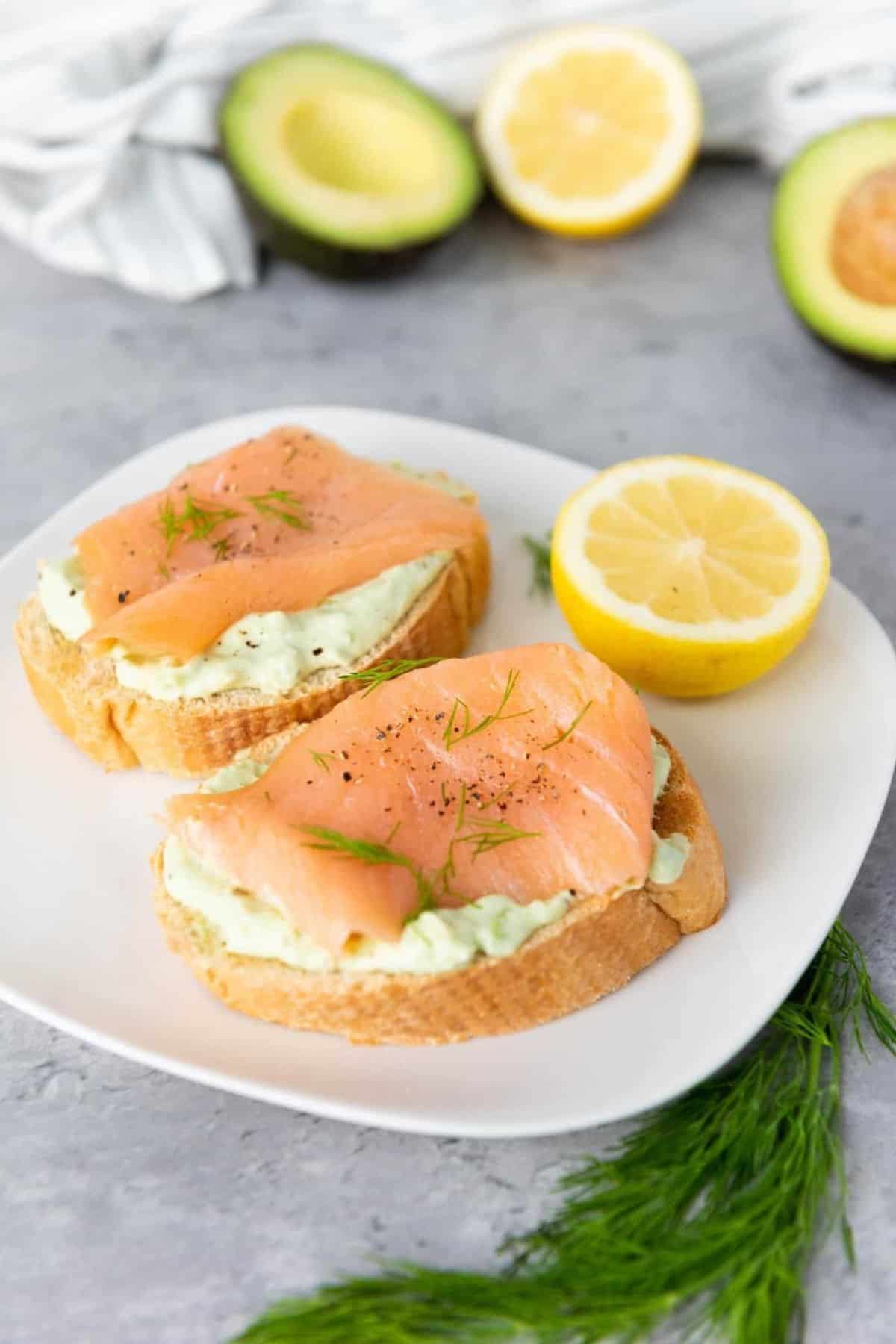 Smoked salmon bruschetta arranged on a plate with lemon slices on the side.