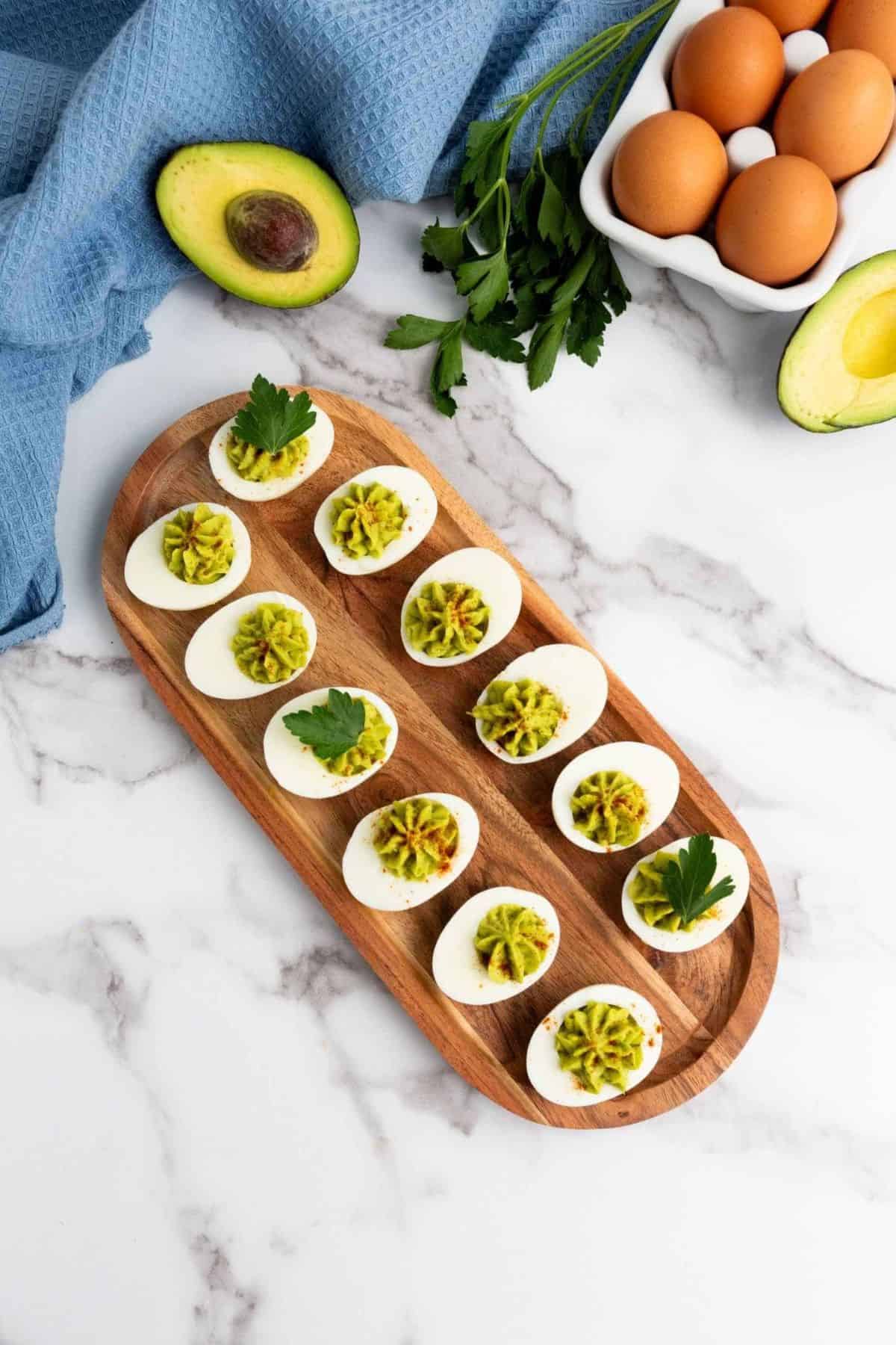 Deviled eggs arranged on a wooden board with sliced avocado on the side.