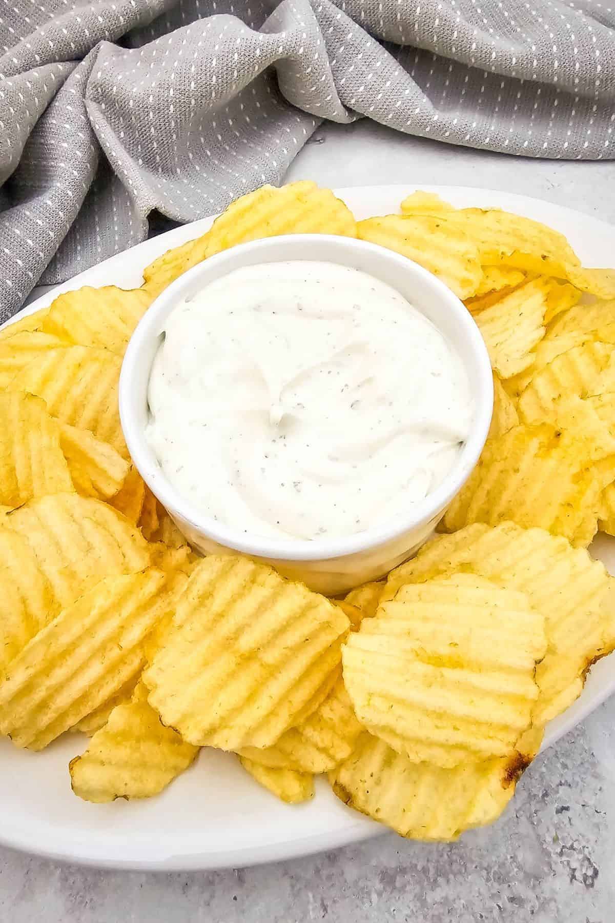 Creamy ranch dip with sour cream in a bowl, surrounded by crispy potato chips.