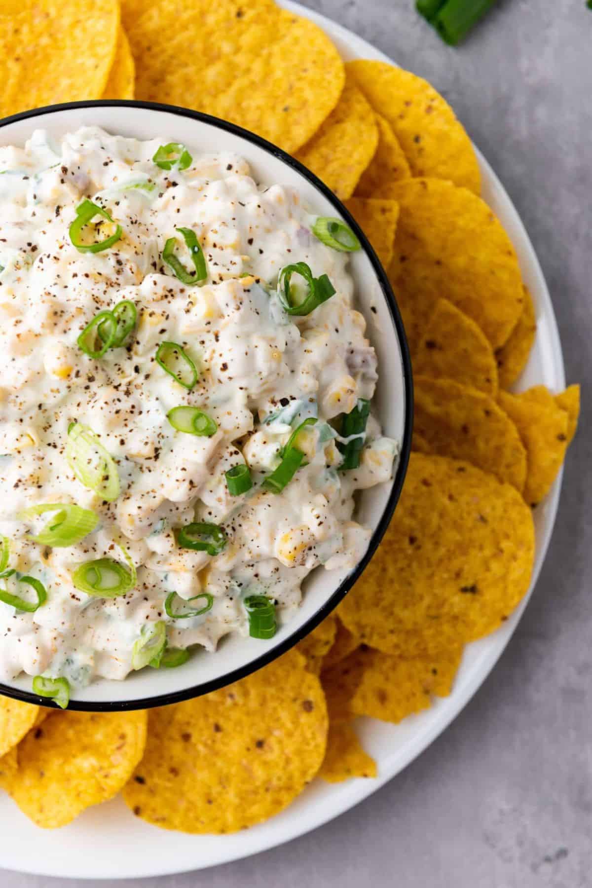 A bowl of creamy corn dip surrounded by tortilla chips ready for dipping.