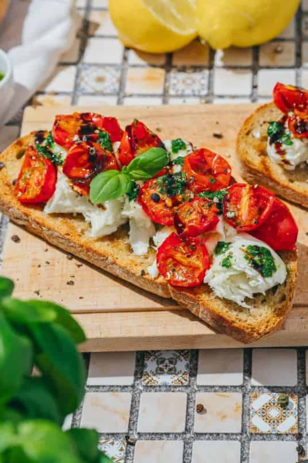 Savory burrata toast topped with roasted tomatoes and basil drizzle, served on a wooden board with decorative plants on the side.