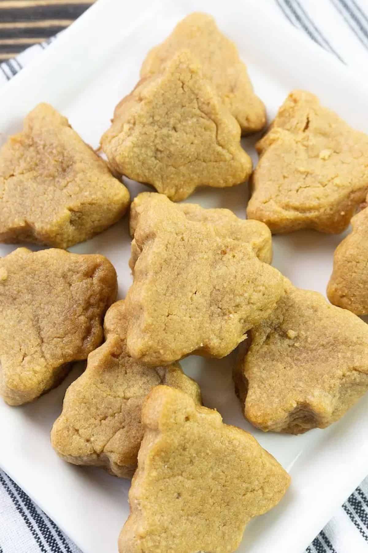 Close-up of peanut butter cookies on a plate with a cloth underneath, showing their golden-brown texture and classic crisscross pattern.