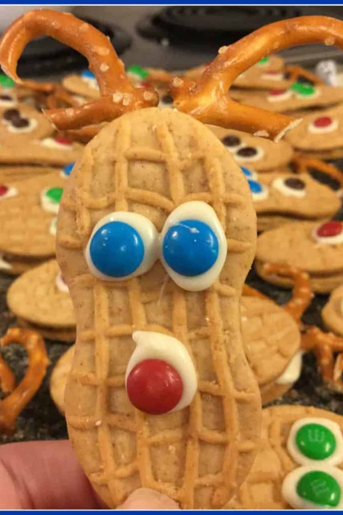 “Close-up of a Nutter Butter Reindeer Cookie with pretzel antlers, with more reindeer cookies blurred in the background.