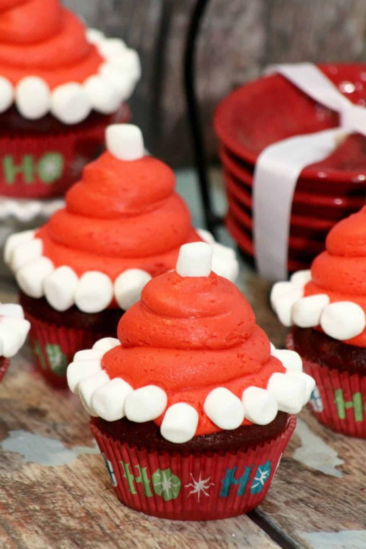 Santa Hat Cupcake placed on a wooden surface with small red bowls blurred in the background.