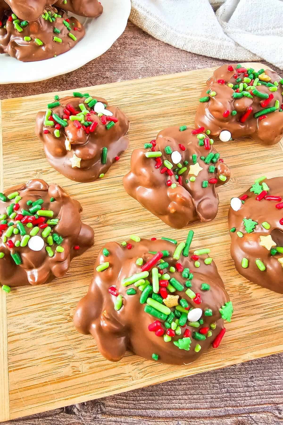 Wooden board filled with Crockpot Christmas Candy clusters, with a linen cloth in the background.