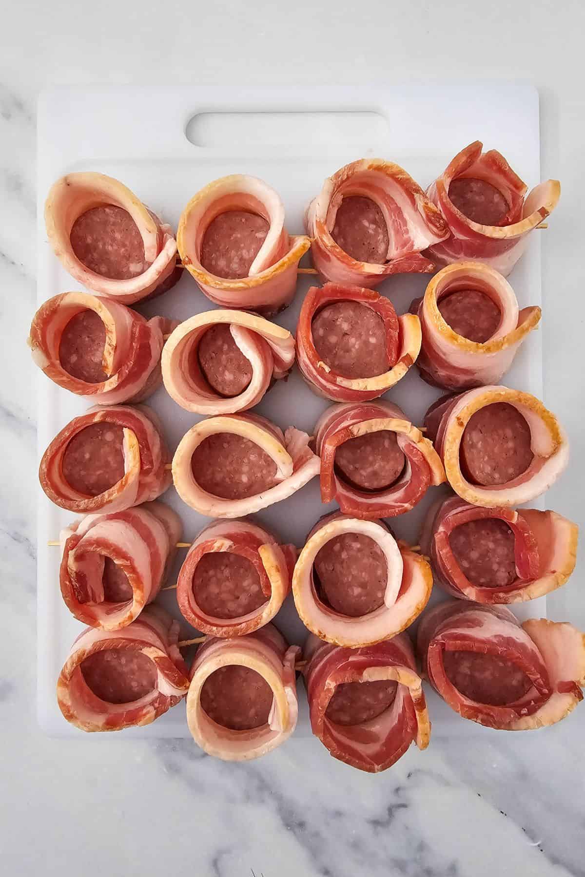 A chopping board lined with uncooked bacon-wrapped pig shots ready to cook.