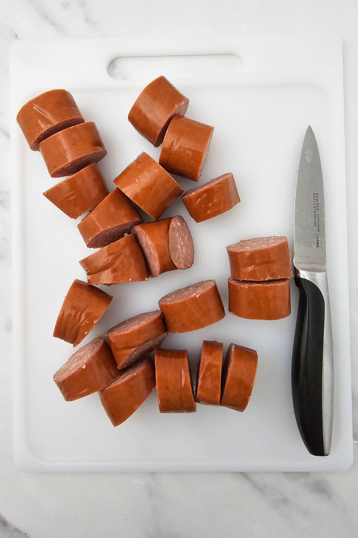 Smoked sausage being sliced on a chopping board with knife on the side.