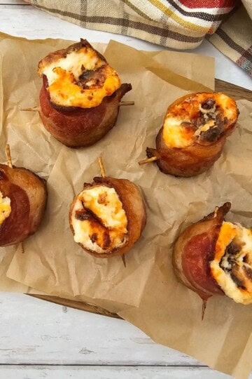 A bacon-wrapped pig shot filled with cheese served on a wooden board lined with parchment paper.