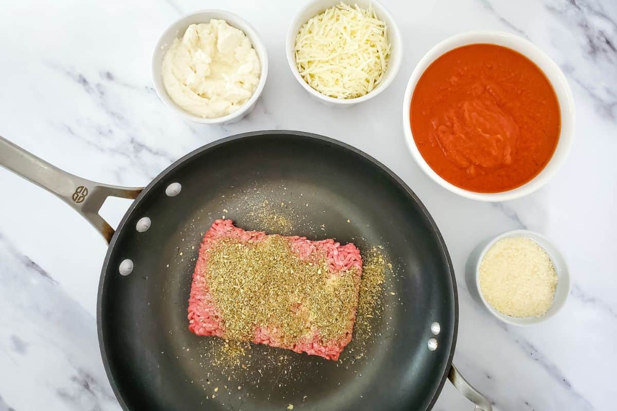 Ground beef being seasoned, with other ingredients around it on the counter.