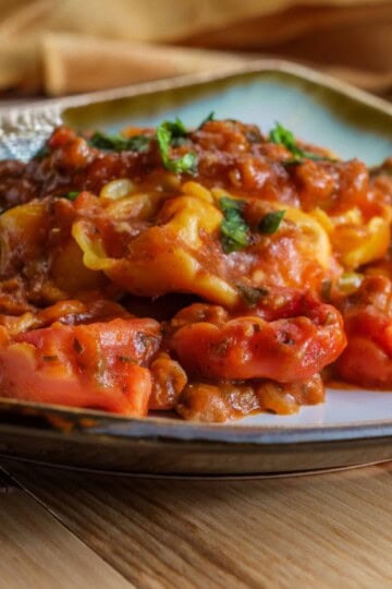 Cheesy Baked Tortellini served on a plate, topped with melted mozzarella and parmesan, with ground beef and sauce visible.