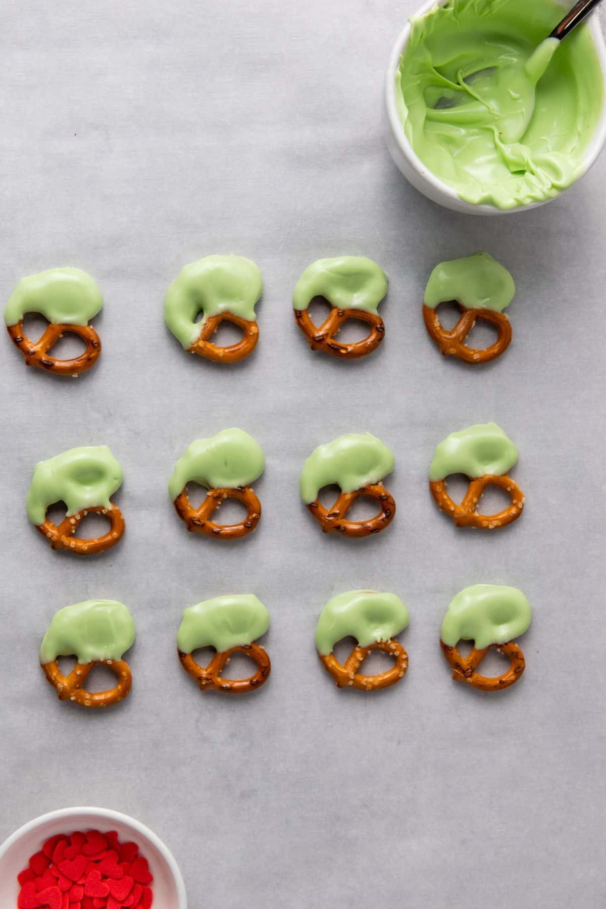 Pretzels being dipped in green candy coating over parchment paper.