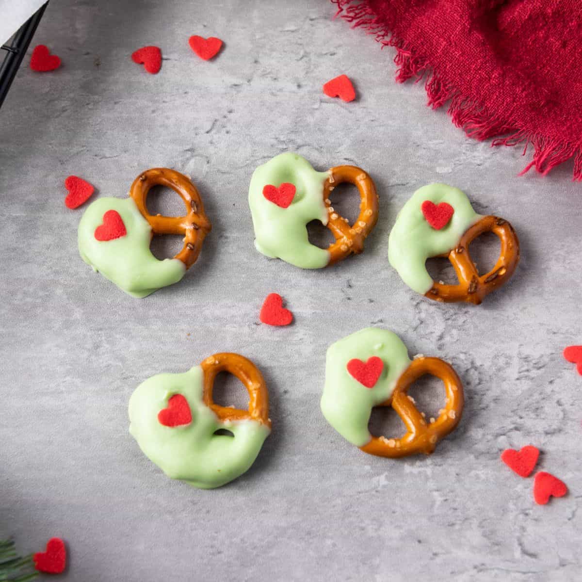 Christmas pretzels on a surface surrounded by heart sprinkles and a red cloth.