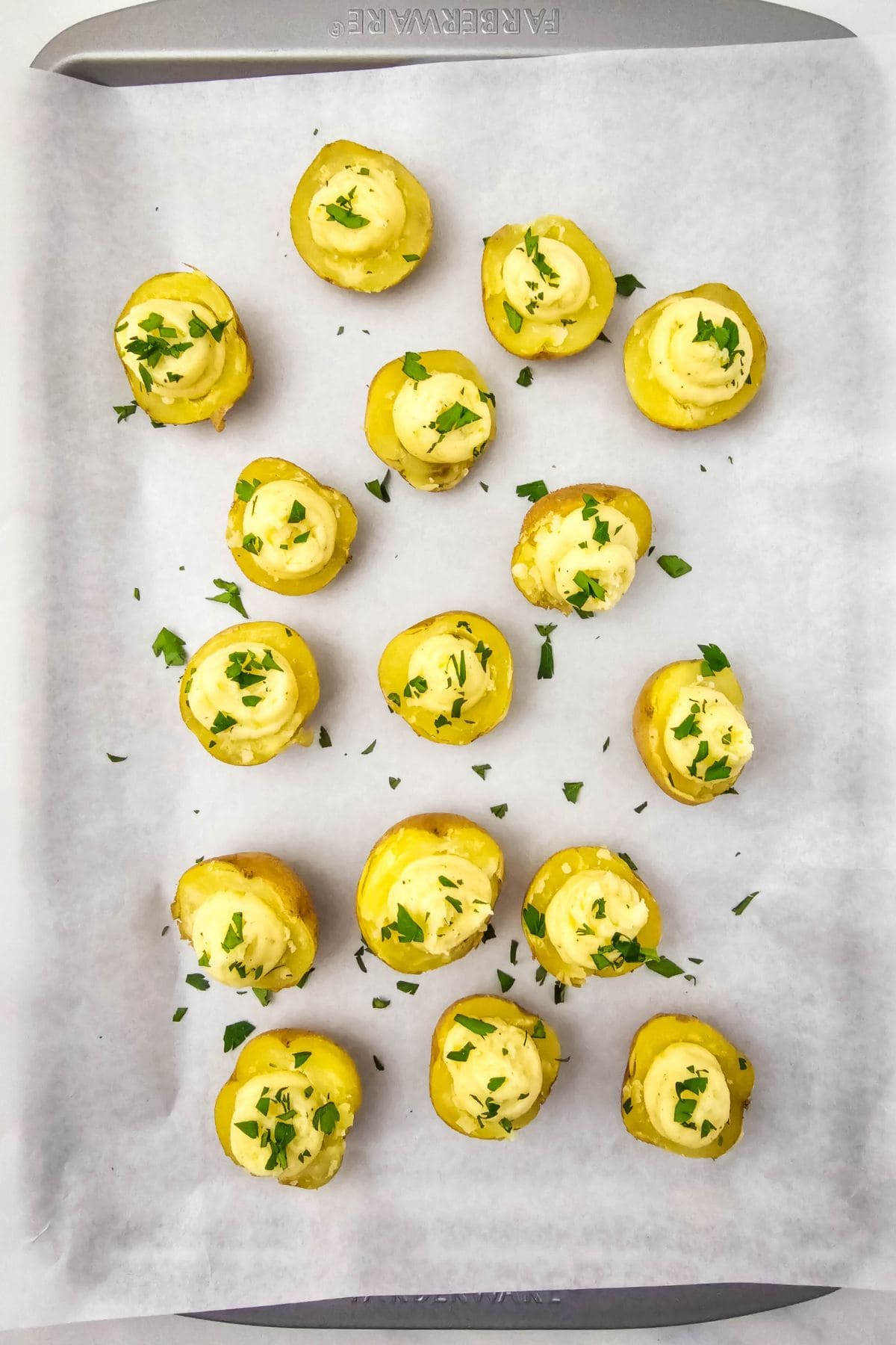 Halved baby potatoes placed on a parchment-lined baking tray, filled with mixture.