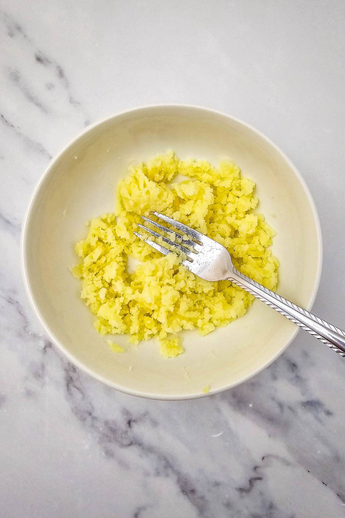 Fork mashing cooked potatoes in a bowl to make deviled potato filling.