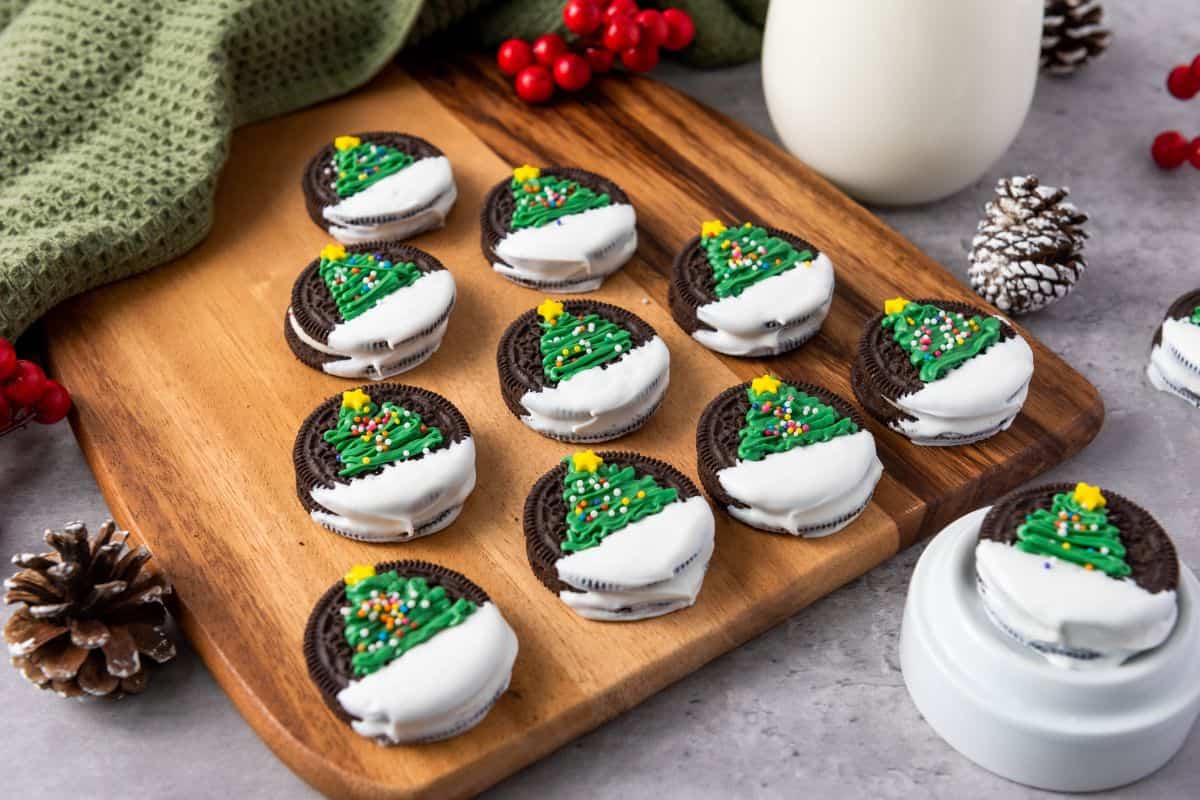 Christmas tree Oreo cookies on a wooden board, placed on a cloth and surrounded by Christmas decorations.