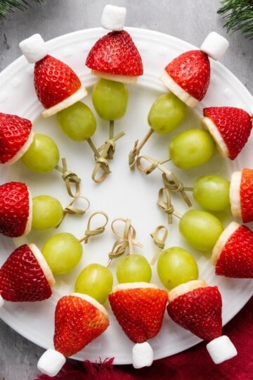 Plate of Green Christmas Man fruit kabobs with holiday decorations on the side for a festive touch.