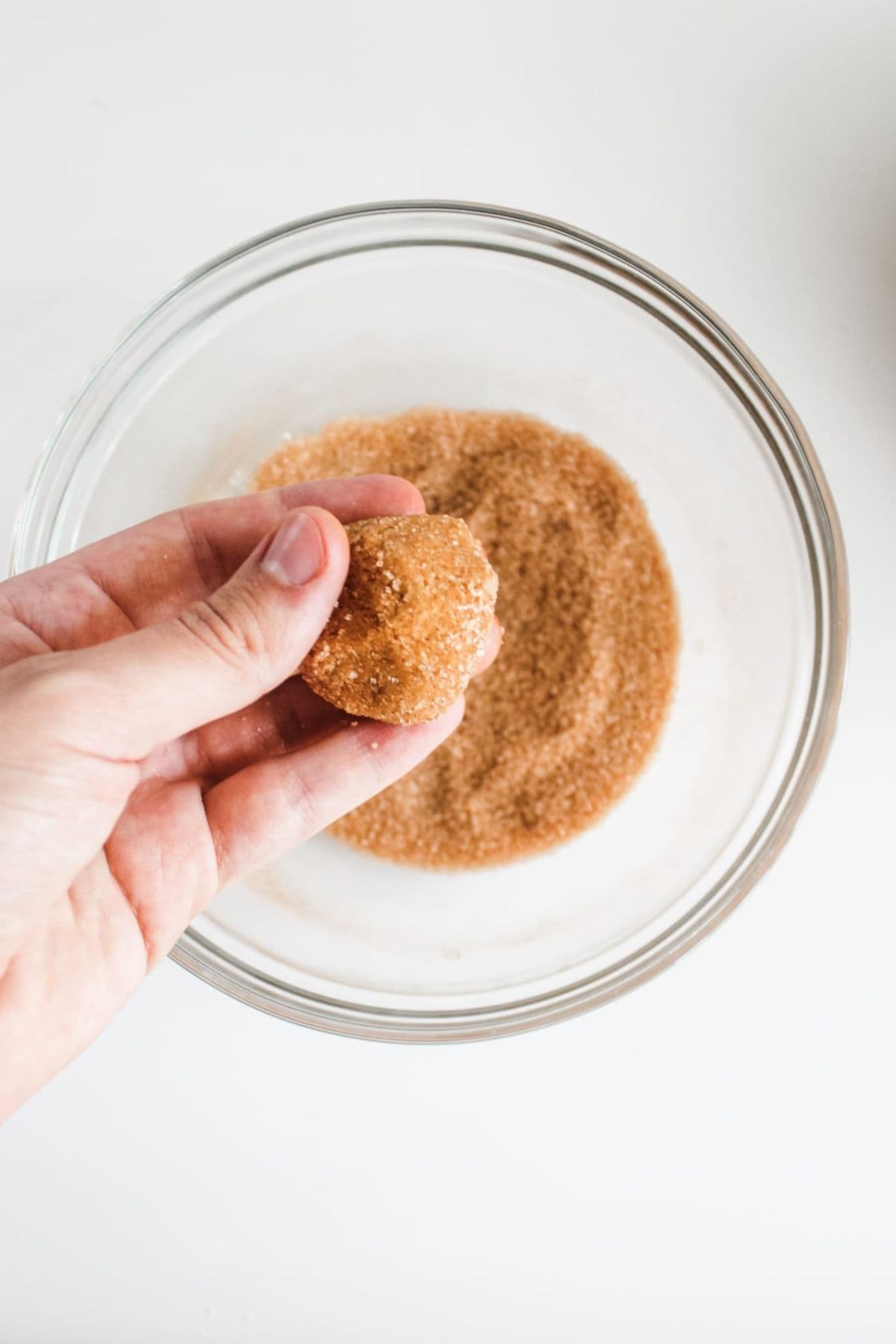 Hand shaping a spiced cookie dough in a large bowl with visible brown sugar and pumpkin pie spice mixture.