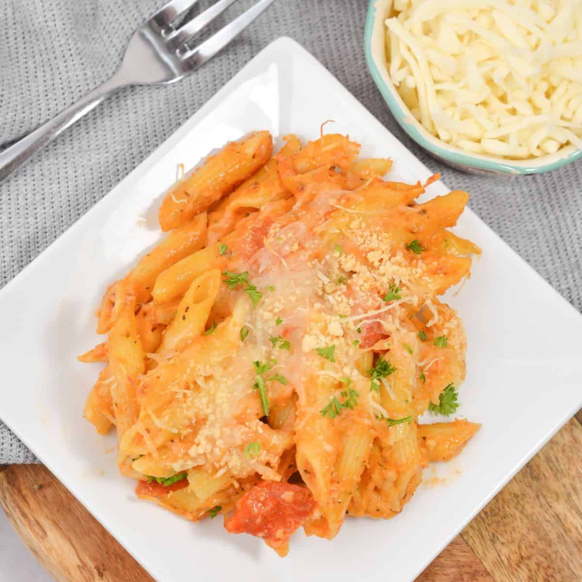 heesy pasta dish on a plate with fork and napkin underneath.