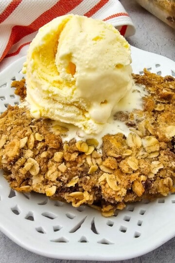 A slice of pumpkin pie topped with a scoop of vanilla ice cream served on a plate.