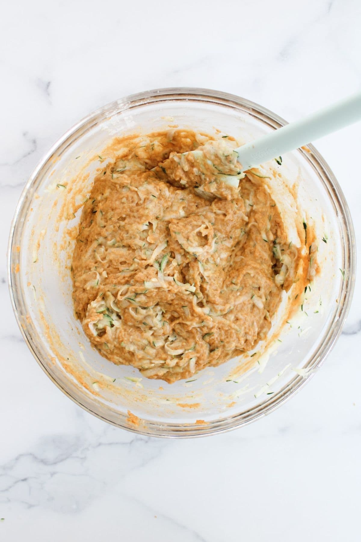Ingredients being gently mixed in a bowl with a spatula resting on the edge.