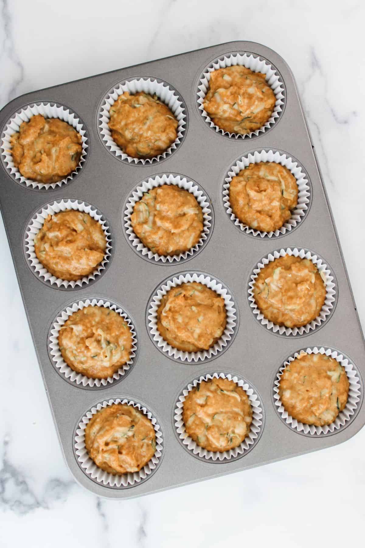 Muffin mixture evenly scooped into a muffin tin, ready for baking.